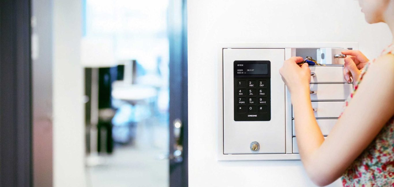 Hand drückt auf ein Türöffnungsgerät mit Ziffernfeld in einem modernen Büro.